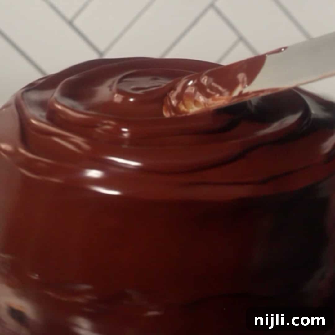 Spreading shiny chocolate ganache over the layered chocolate mousse cake for a smooth finish.