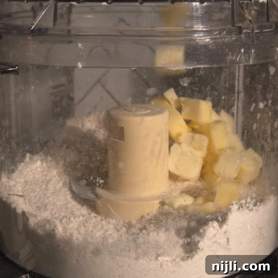Mixing flour and cubed butter in a food processor to make shortbread crust for chocolate pecan pie bars.