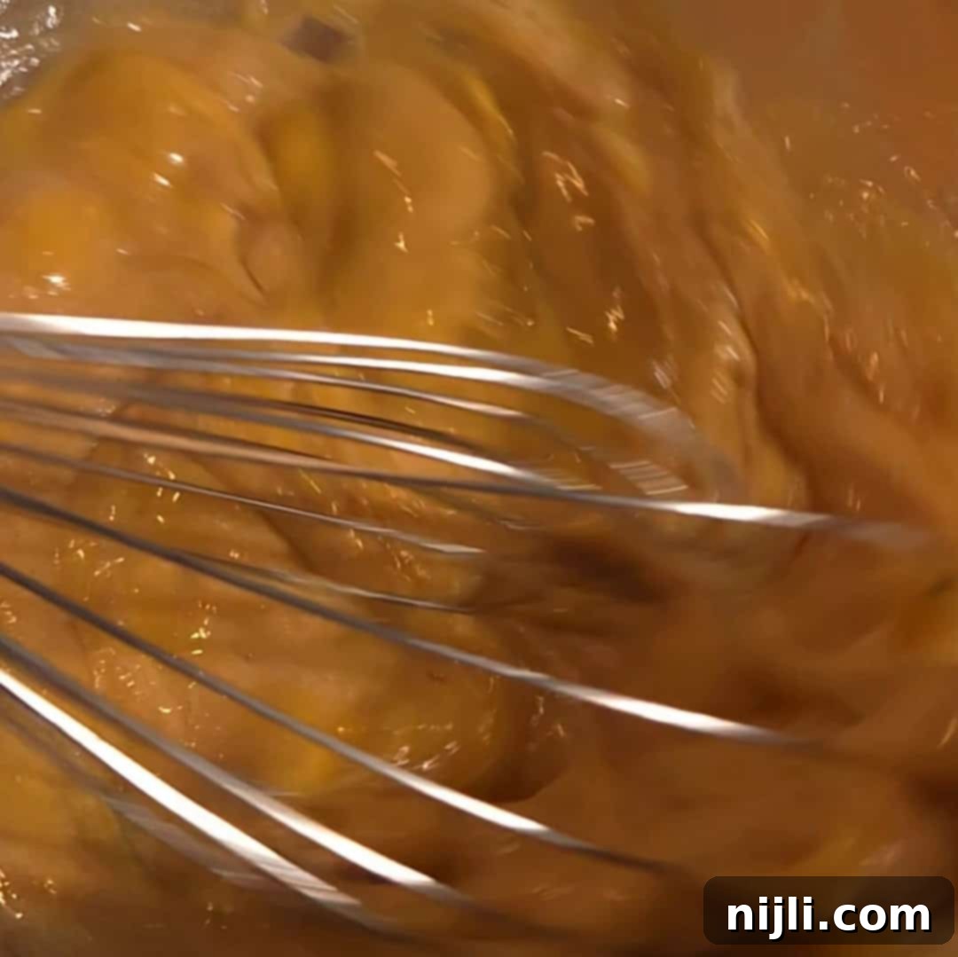 Whisking eggs and brown sugar together to create gooey pecan pie filling for chocolate pecan bars.