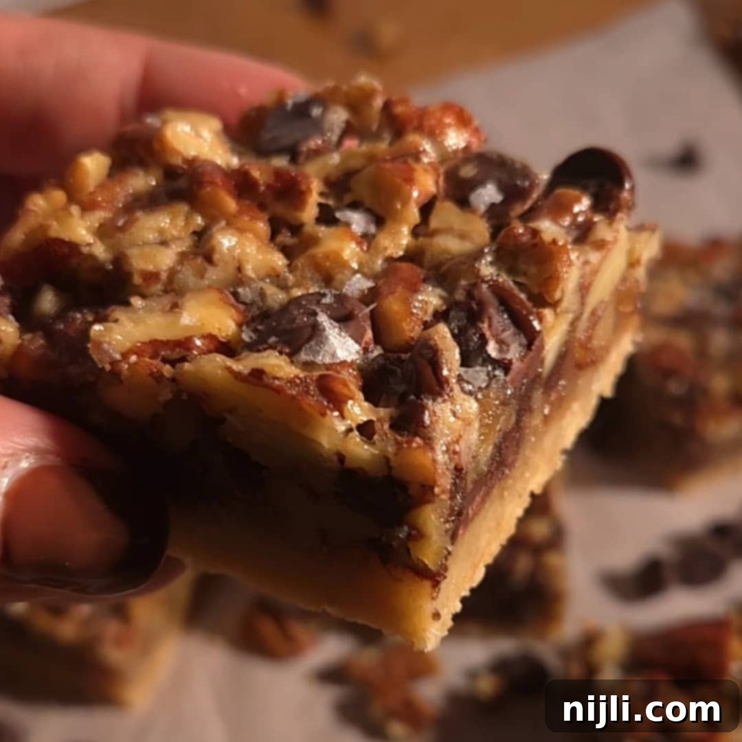 Gooey square of chocolate pecan pie bar with thick filling and a golden crust.