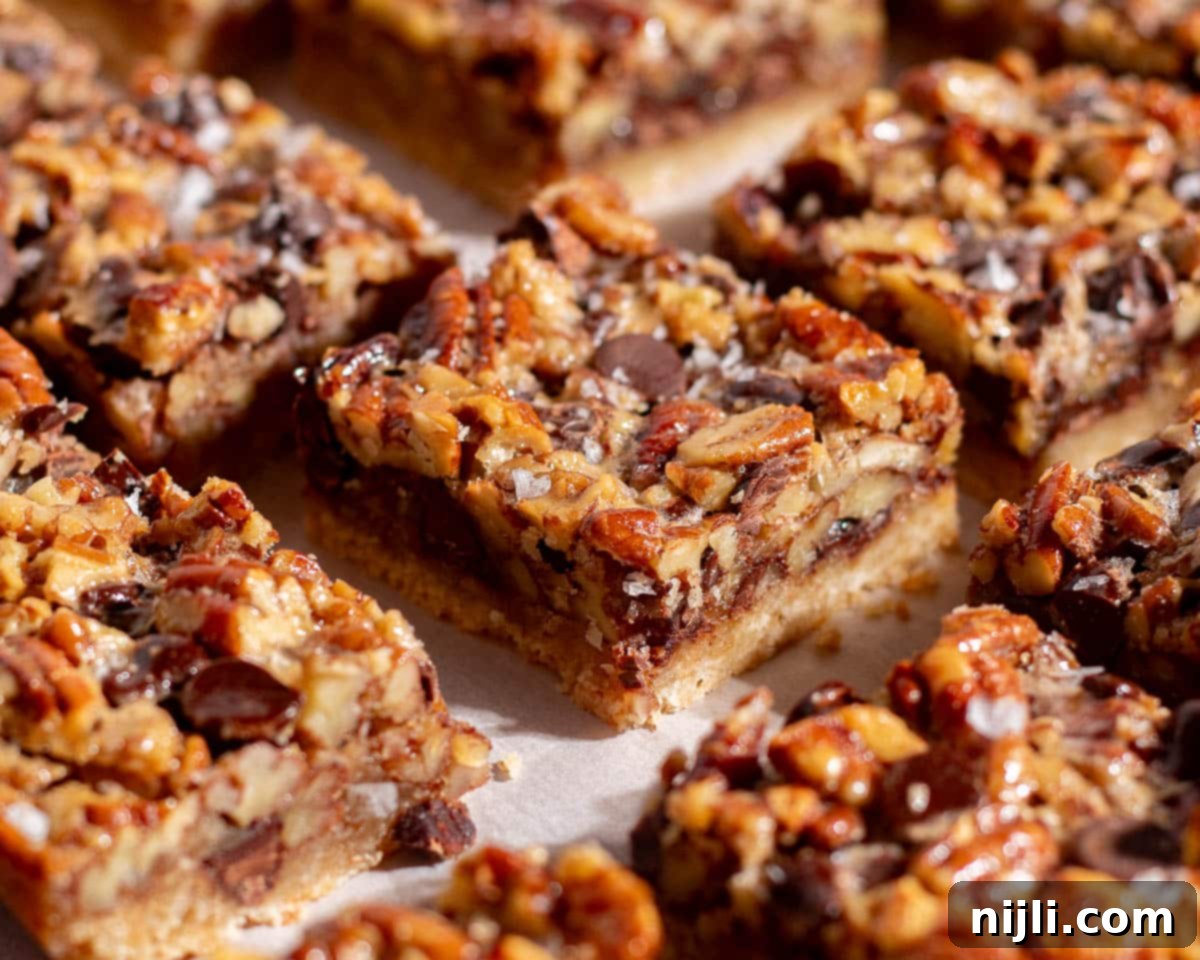 Close-up of baked chocolate pecan pie bars with layers of chocolate chips, toasted pecans, and golden shortbread crust.