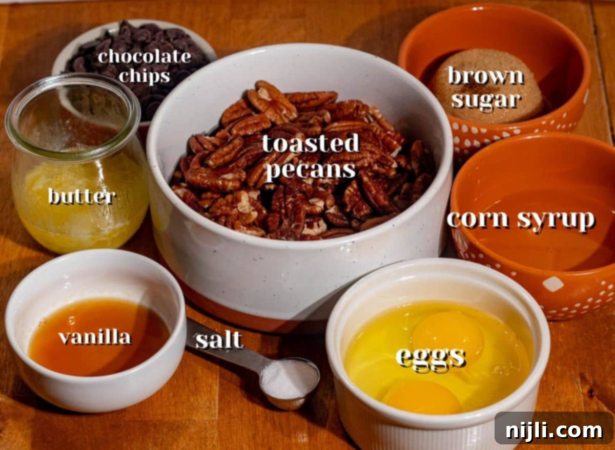 Ingredients for chocolate pecan pie bars including brown sugar, corn syrup, eggs, butter, toasted pecans, and chocolate chips on a wooden table.