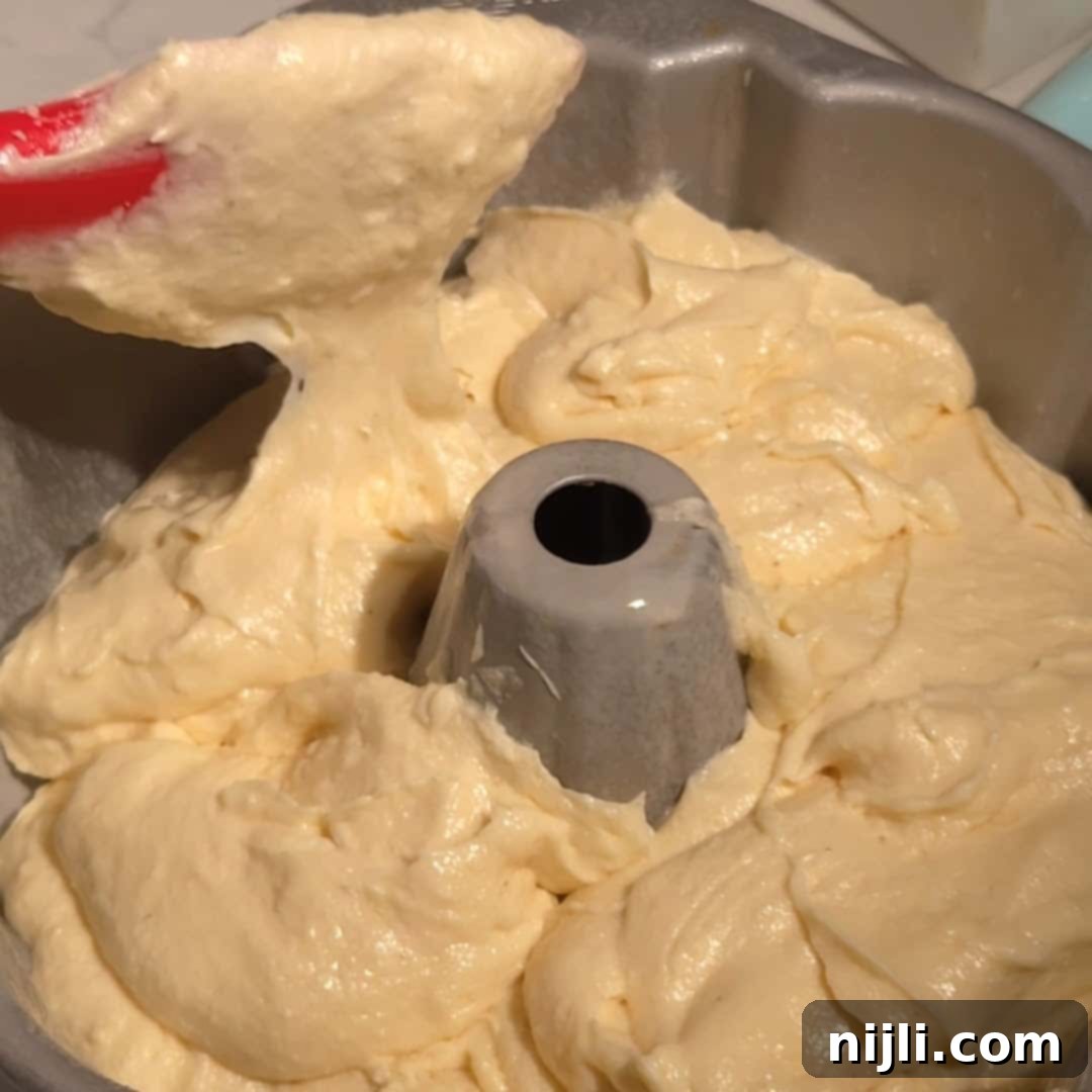 Carefully spreading the thick eggnog pound cake batter into a prepared Bundt pan before baking.
