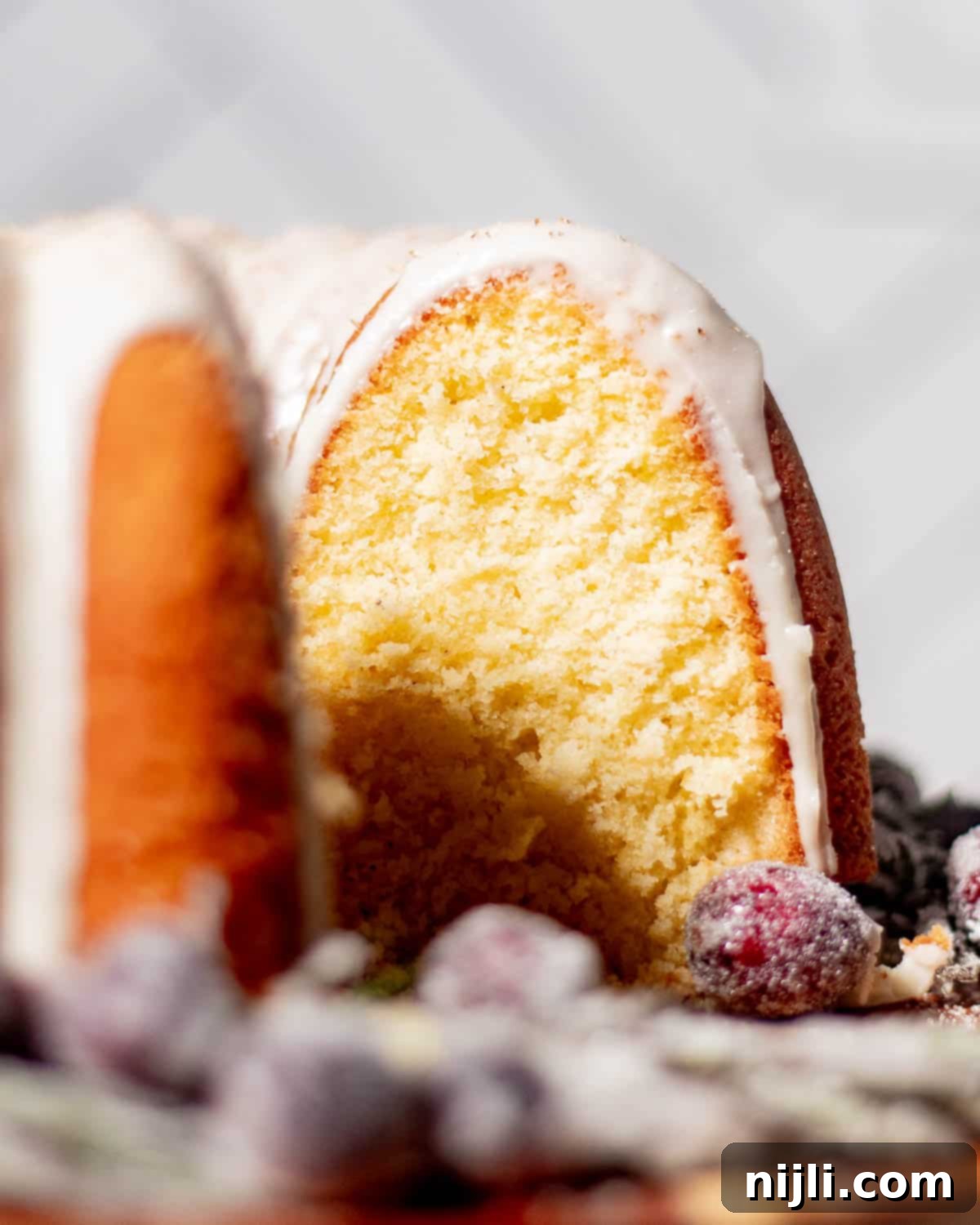 Close-up of moist eggnog pound cake crumb with white glaze and sparkling sugared cranberries, perfect for Christmas baking.