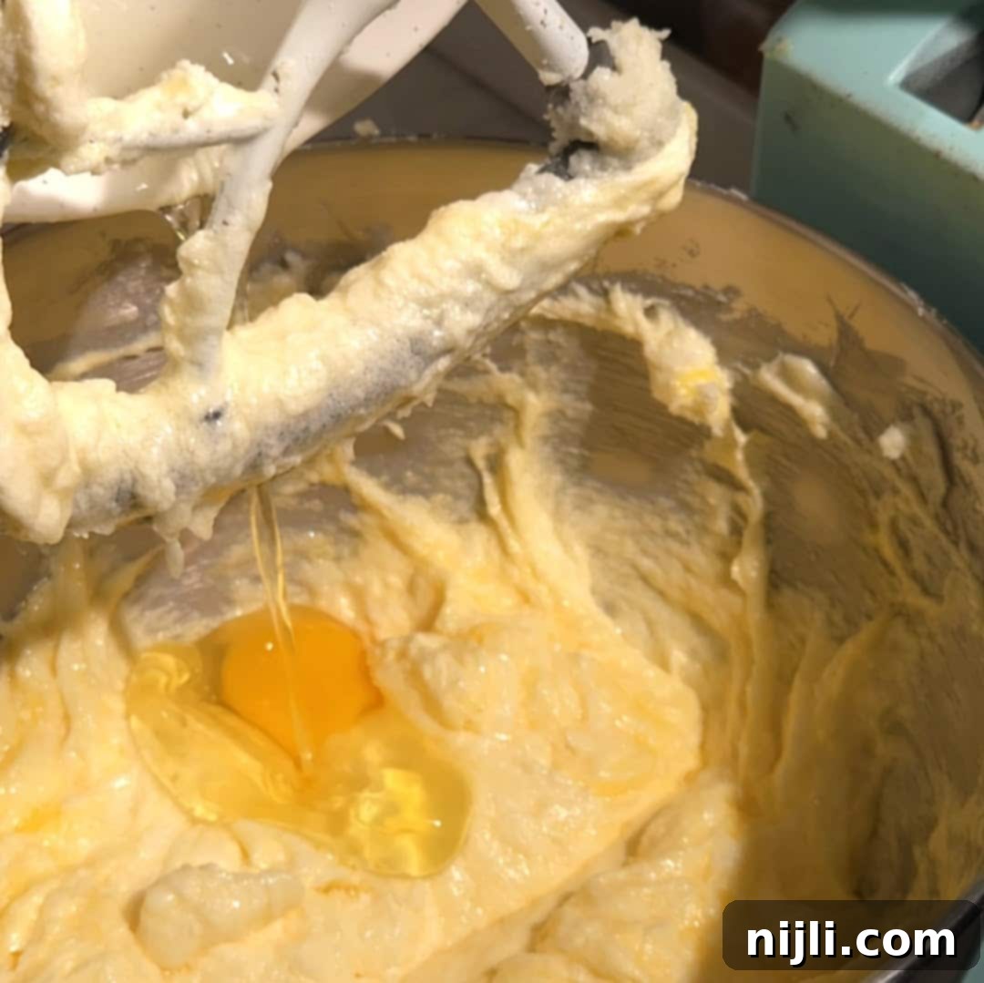Adding eggs one at a time to the butter and sugar mixture, followed by vanilla and rum extracts.
