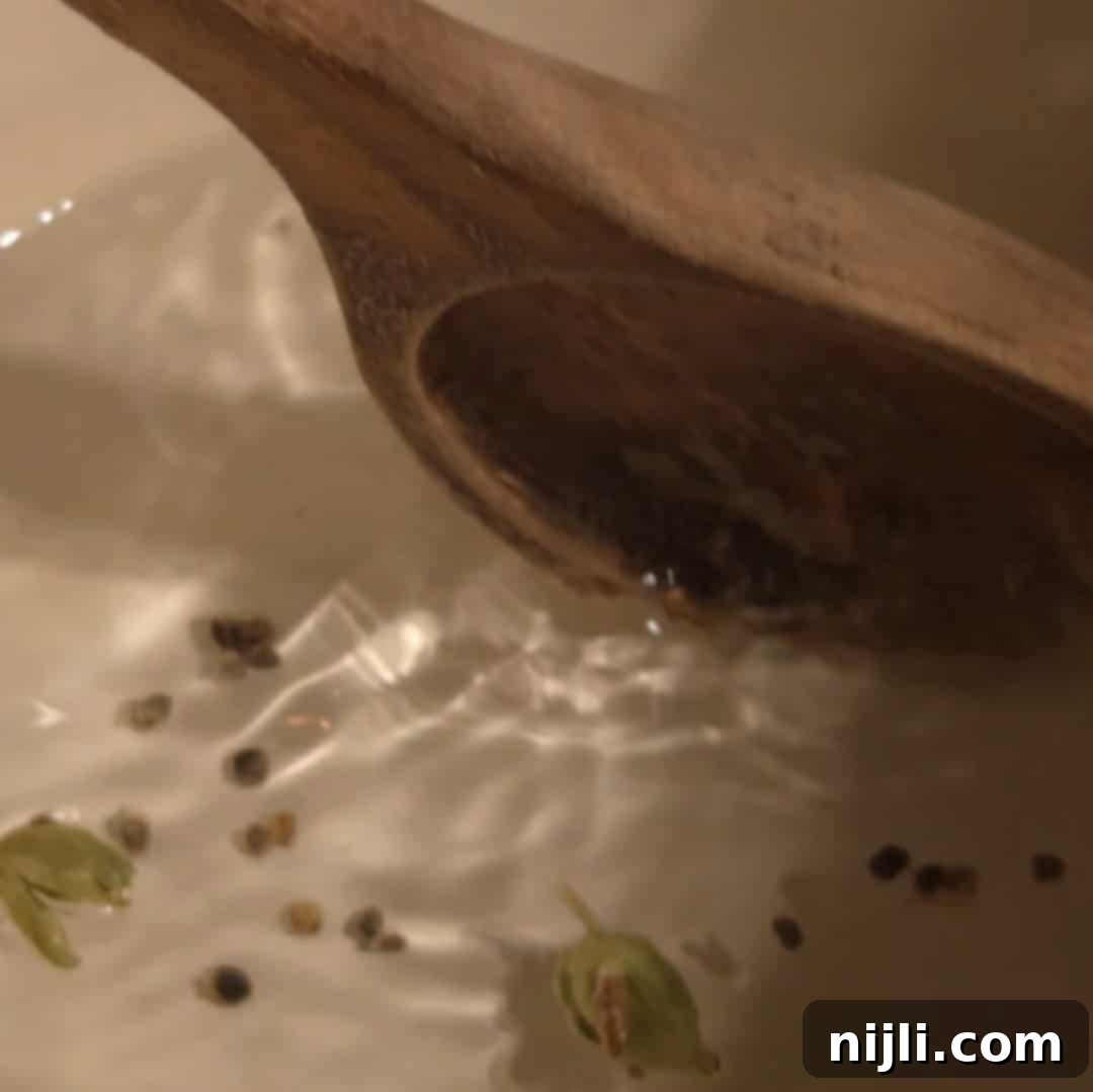 Stirring crushed cardamom pods in water inside a white saucepan to start the cardamom syrup base.