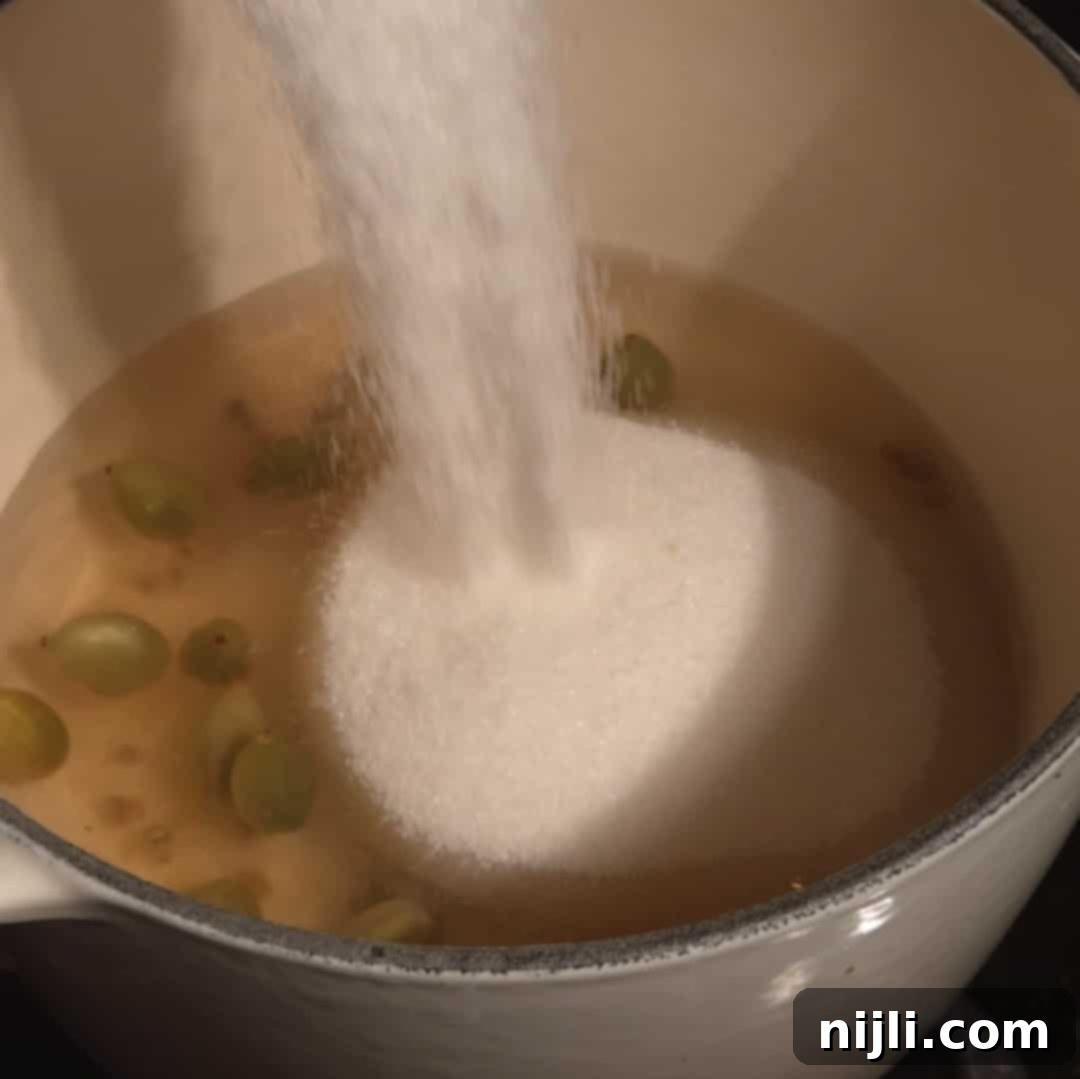 Pouring sugar into simmering water with cardamom pods to dissolve and create cardamom simple syrup.