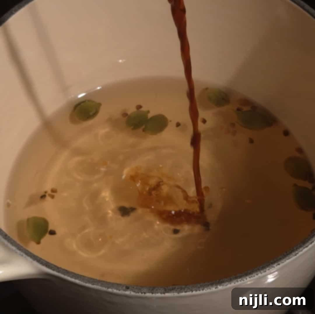 Adding vanilla extract to the saucepan of hot cardamom syrup for extra flavor.