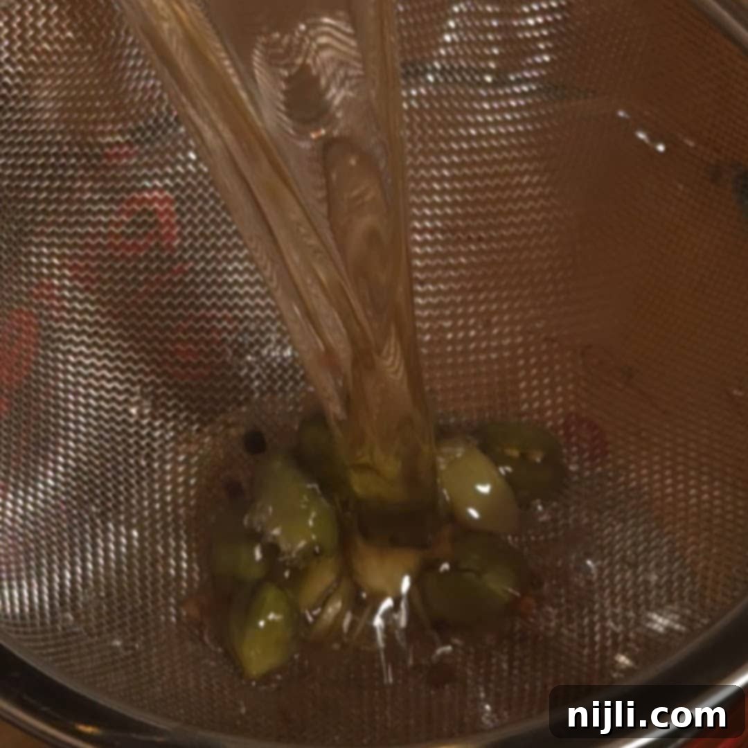Straining the finished cardamom syrup through a fine mesh sieve to remove cardamom pods.