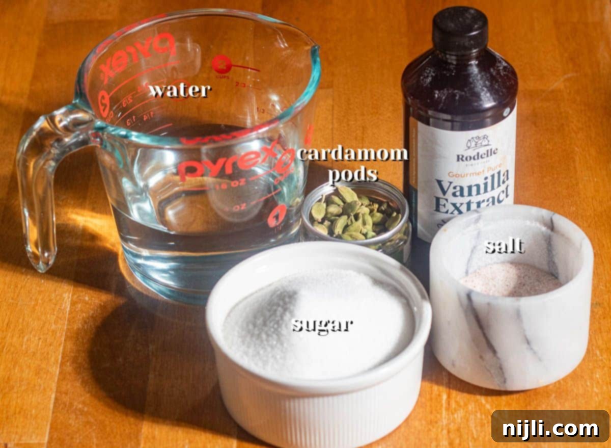 Overhead shot of cardamom syrup ingredients including sugar, water, cardamom pods, vanilla extract, and salt on a wooden surface.